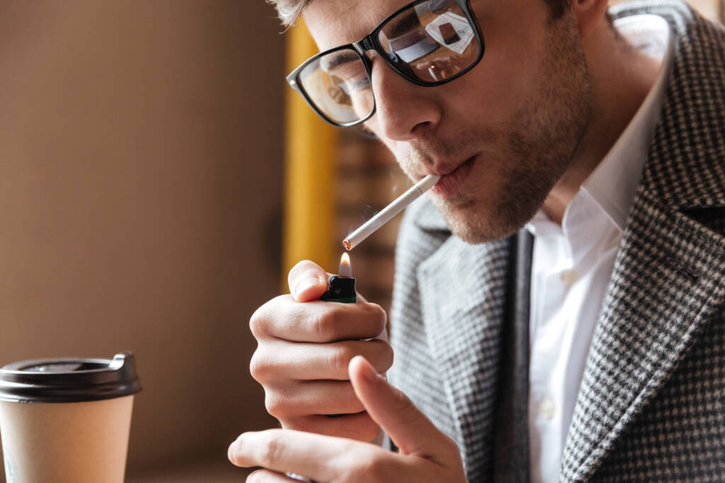 Man lighting a cigarette with a coffee cup