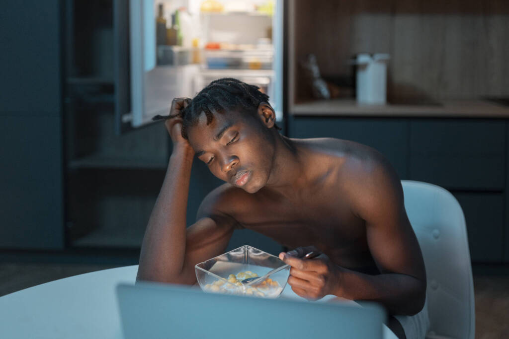 Man in front of laptop screen eating late at night